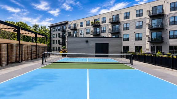 A tennis court is surrounded by apartment buildings.