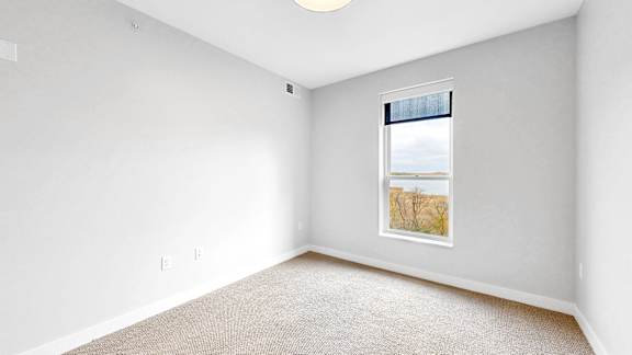 A room with a carpeted floor and a window with a view of a tree.