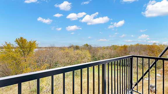 A balcony with a metal railing overlooks a field with trees.