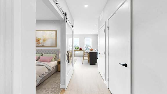A white hallway with a bedroom and a kitchen visible through the door.