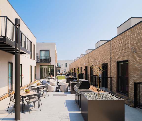 A patio with tables and chairs is surrounded by brick buildings.