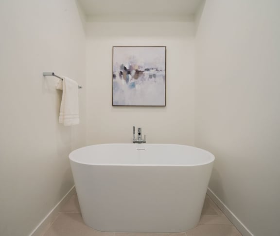 A white bathtub sits in a bathroom with a painting on the wall.