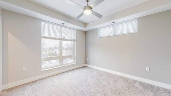 A room with a ceiling fan and large windows.