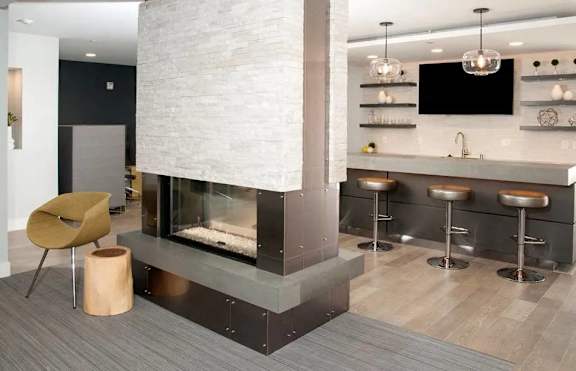 A modern kitchen with a stone fireplace and bar stools.