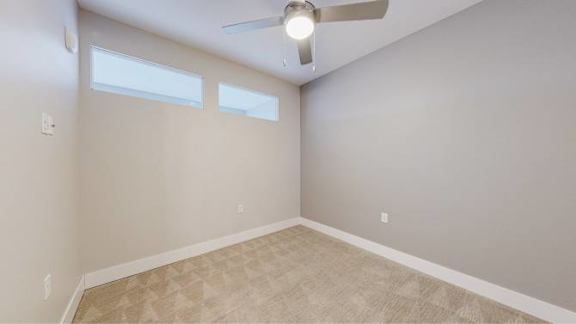 A room with a ceiling fan and two windows.