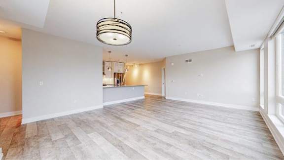 A large, empty room with light wood flooring and a pendant light hanging from the ceiling.