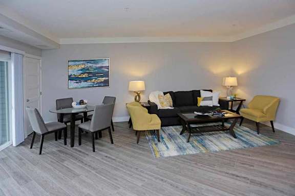 A living room with a grey couch, a yellow chair, a black chair, a coffee table, and a painting on the wall.