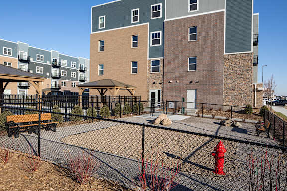 A playground area with a red fire hydrant and a fence in front of apartment buildings.