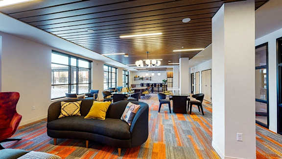 A large room with a long couch and a red chair at The Bessemer at Seward Commons Apartments, Minneapolis, Minnesota