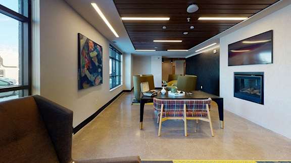 A modern living room with a brown couch, a wooden table, and a painting on the wall at The Bessemer at Seward Commons Apartments, Minneapolis, MN,  55404