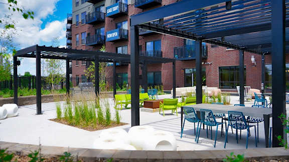 A patio area with tables and chairs is covered by a black awning at The Bessemer at Seward Commons Apartments, Minneapolis, Minnesota