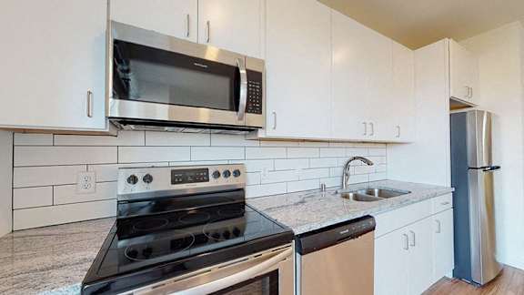 A kitchen with a stove, microwave, and refrigerator at The Bessemer at Seward Commons Apartments, MN, 55404