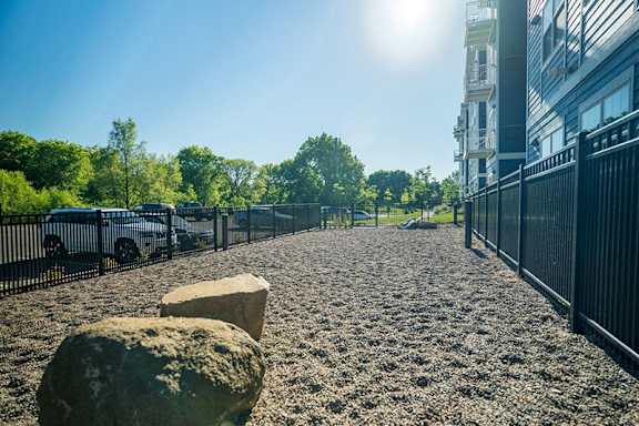 A sunny day in a park with a gravel path, trees, and a fence at The Barnum Apartments, MN, 55110