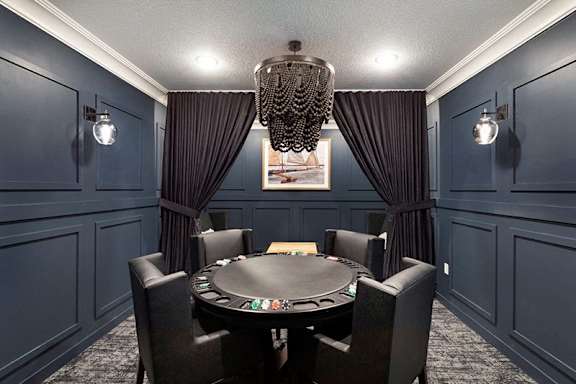 A black poker table is surrounded by chairs in a room with dark walls at The Barnum Apartments, White Bear Lake