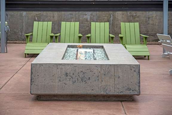 A concrete fountain in the middle of a patio surrounded by green chairs.
