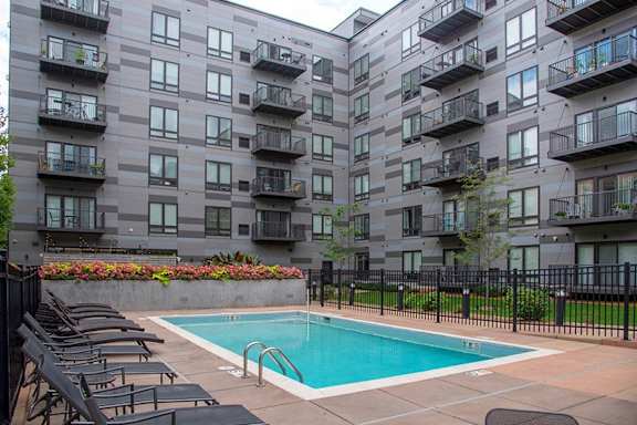 A pool surrounded by chairs and apartment buildings.