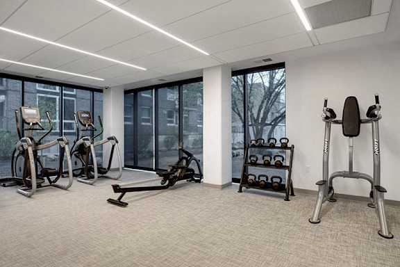 A gym with a row of treadmills, elliptical machines, and a weight rack.at Viridium Apartments, Minneapolis