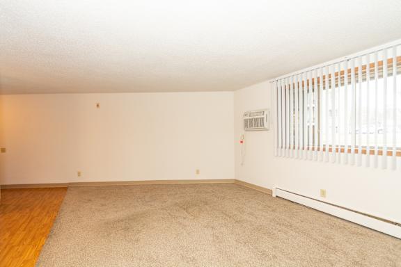 A room with a carpeted floor and a window with blinds.