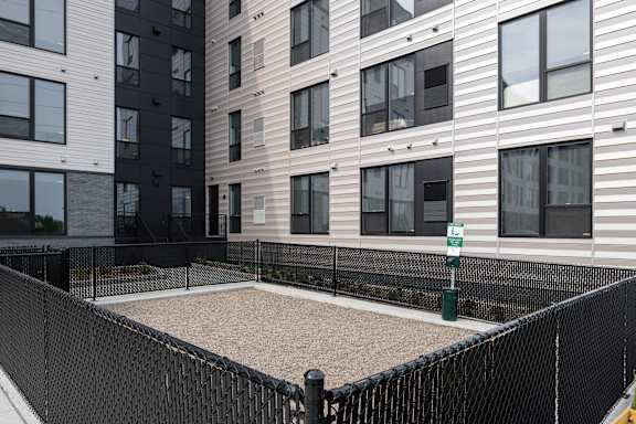 A black fenced sandbox in front of apartment buildings.