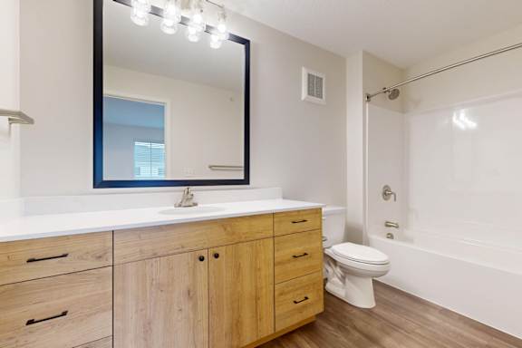 A bathroom with a white counter top and wooden cabinets.
