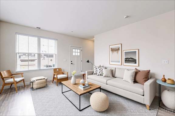 A living room with a grey couch, a coffee table, and a window with blinds.
