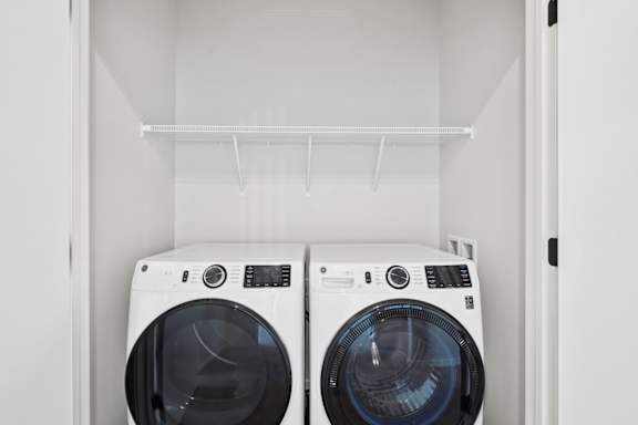 Two white front loading washing machines in a white laundry room.
