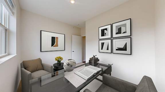 A living room with a grey couch, a glass table with a book and a vase of flowers on it, and framed artwork on the wall.