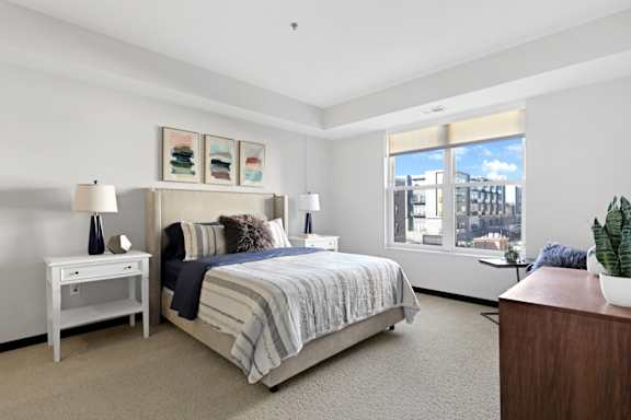 A bedroom with a large bed, a nightstand, and a window overlooking the city.