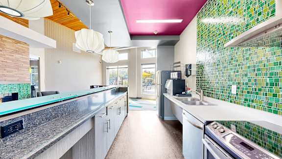 A modern kitchen with a green tiled backsplash and white cabinets.