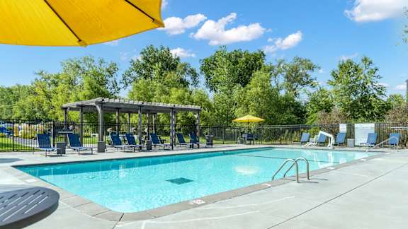 A sunny day at the pool with a yellow umbrella providing shade.