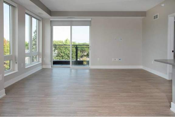 A spacious room with wooden flooring and large windows.