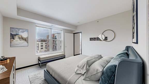 A bedroom with a bed, a chair, and a window overlooking a building.