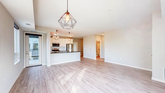 an empty living room with a kitchen in the background
