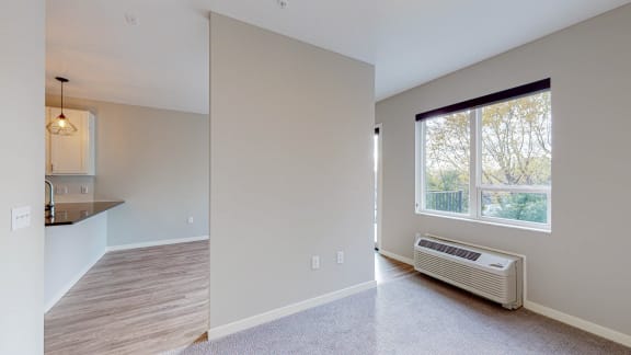 an empty room with a large window and a kitchen in the background