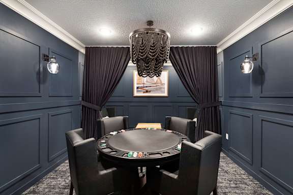A black poker table is surrounded by black chairs in a room with dark walls at The Barnum Apartments, Minnesota, 55110