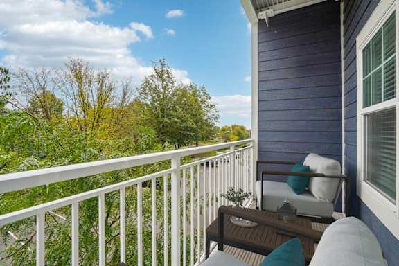A balcony with a white railing, a brown table, and a white chair with a blue cushion.