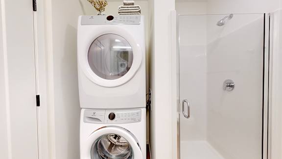A white washing machine and dryer stacked on top of each other in a small laundry room.