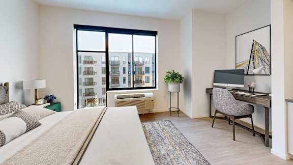 A bedroom with a large bed, a desk with a chair, and a window overlooking a cityscape.