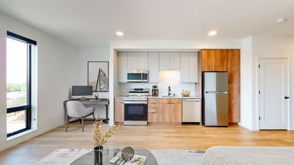 a living room with a kitchen with a refrigerator and a sink