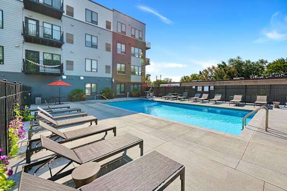 a swimming pool with lounge chairs and umbrellas in front of an apartment building