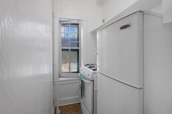a small white kitchen with a window and a white refrigerator