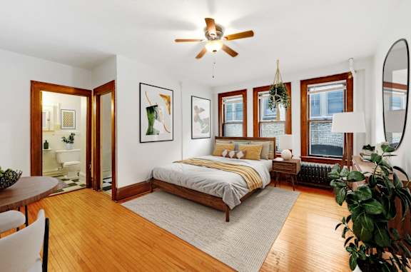 A bedroom with a bed, a ceiling fan, and a potted plant.