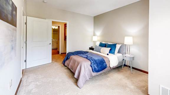 A bedroom with a bed, two lamps, and a carpeted floor.