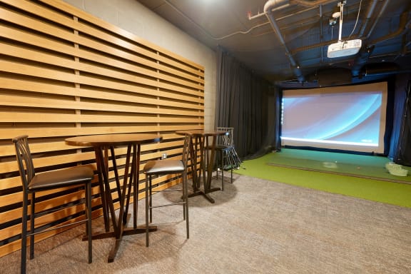golf simulator room with chairs, artificial turf and a projector screen