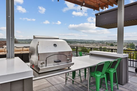 an outdoor kitchen with a grill and a table with green chairs