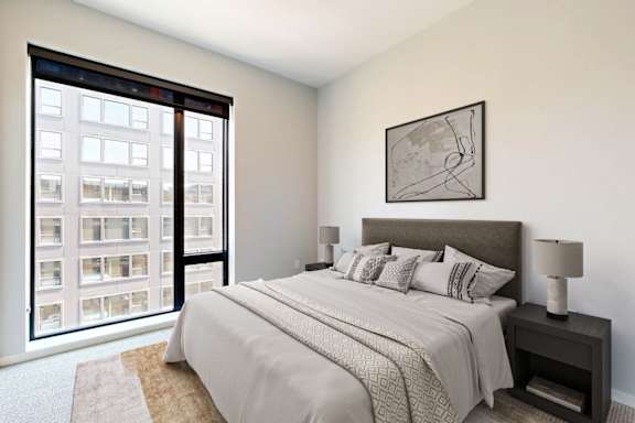 A bedroom with a large bed and a large window overlooking a building.