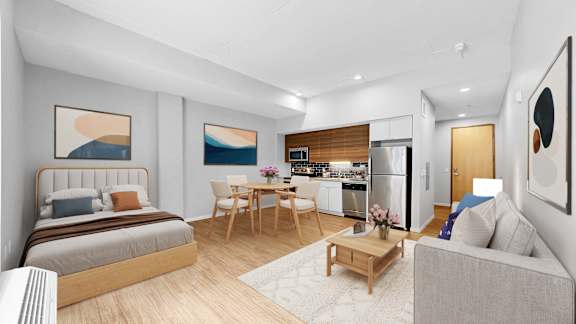 A modern living room with a bed, a couch, a dining table, and a kitchen area in the background.