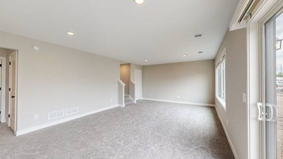 A spacious room with a carpeted floor and a staircase leading to another level.
