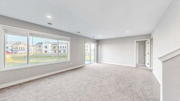 A spacious room with a carpeted floor and large windows overlooking a residential area.
