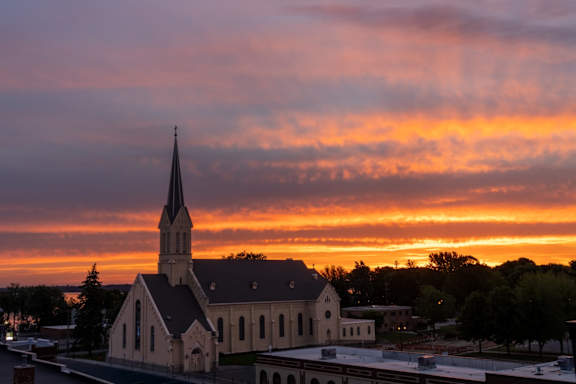 A church with a steeple is silhouetted against a sunset sky.